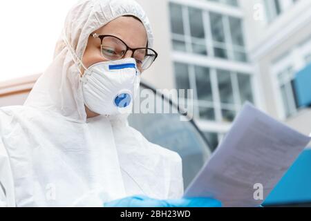 Ritratto di stanco esaurito medico femminile, scienziato o infermiere che indossa maschera facciale e nocciolo biologico ppe tuta lettura Who protocollo di trattamento o. Foto Stock