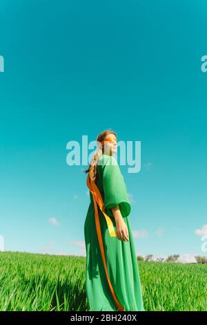 Giovane donna bendata che indossa un vestito verde in piedi in un campo Foto Stock