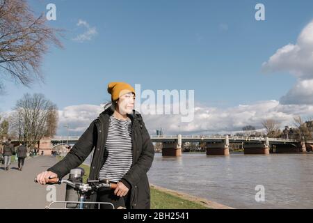 Donna con bicicletta sulla riva del fiume, Francoforte, Germania Foto Stock