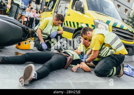 I paramedici aiutano a soccorrarsi dopo un incidente con lo scooter Foto Stock