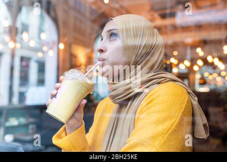 Giovane donna che indossa hijab bere frullato in un caffè Foto Stock