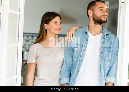 Giovane coppia attraente che si trova insieme nella porta a casa e guardando fuori Foto Stock