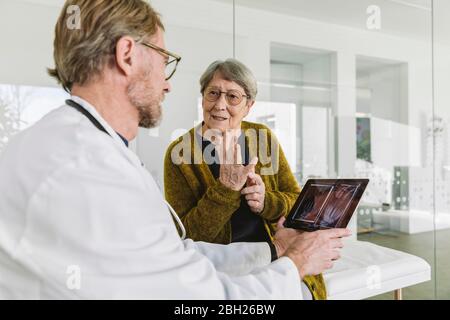 Medico che discute l'immagine radiografica della mano rotta con il paziente anziano Foto Stock