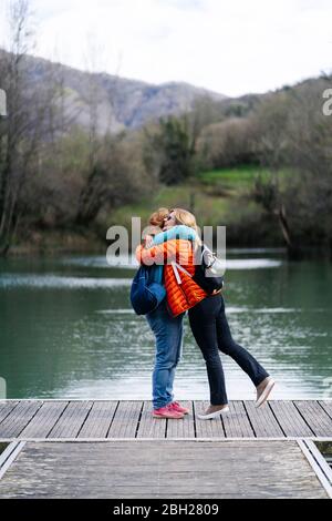 Due donne felici con zaini in piedi sul molo abbracciano l'un l'altro, Valdemurio Reservoir, Asturias, Spagna Foto Stock