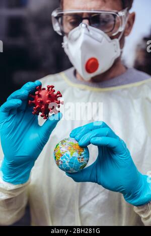 Operatore sanitario che tiene modello di Corona Virus e un mini globo Foto Stock