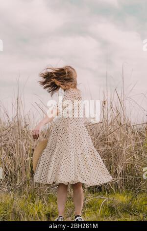 Donna in abito vintage che le lancia i capelli in un campo remoto in campagna Foto Stock