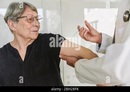 Medico che inietta il vaccino nel braccio di un paziente anziano Foto Stock