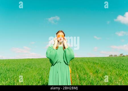 Giovane donna bendata che indossa un vestito verde in piedi in un campo Foto Stock