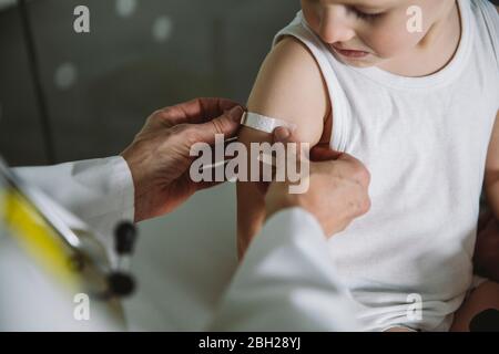 Pediatra che mette la banda-aiuto sul braccio del bambino dopo la vaccinazione Foto Stock