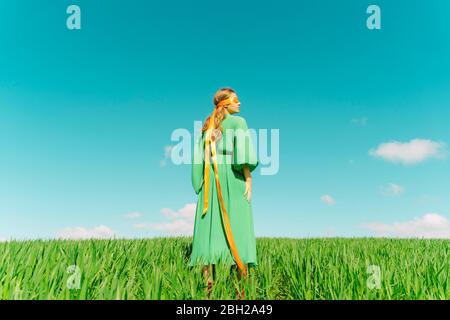 Giovane donna bendata che indossa un vestito verde in piedi in un campo Foto Stock