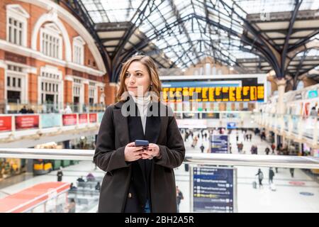 Donna alla stazione ferroviaria con un telefono cellulare, Londra, Regno Unito Foto Stock