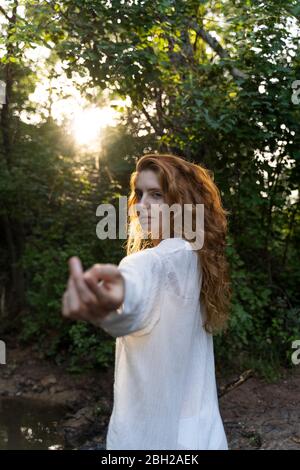 Giovane donna dai capelli rossi che le tira fuori le mani nella foresta Foto Stock