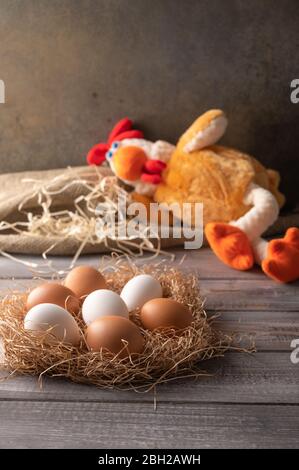 Uova di pollo marroni e bianche in un nido di paglia su sfondo di legno. Accanto ad un giocattolo di pollo che dorme. Orientamento verticale Foto Stock