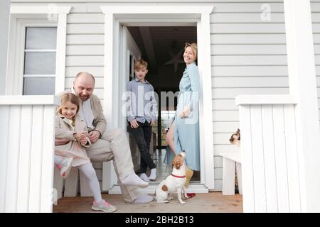 Famiglia felice con gatto e cane sul portico della loro casa Foto Stock