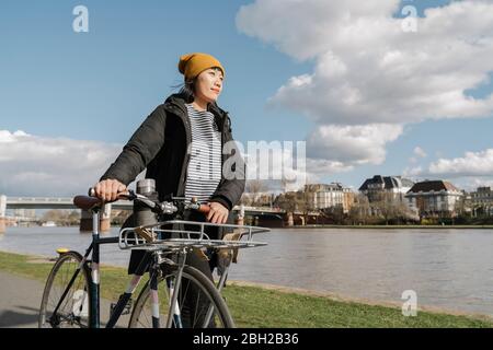 Donna con bicicletta sulla riva del fiume, Francoforte, Germania Foto Stock