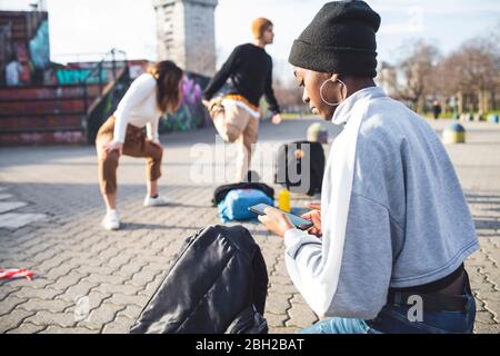 Giovani ballerini che provano in un parco di sci, giovane donna che usa lo smartphone Foto Stock