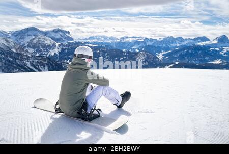 Donna sorridente seduta con snowboard sul punto panoramico e vista a distanza Foto Stock