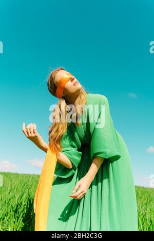 Giovane donna bendata che indossa un vestito verde in piedi in un campo Foto Stock