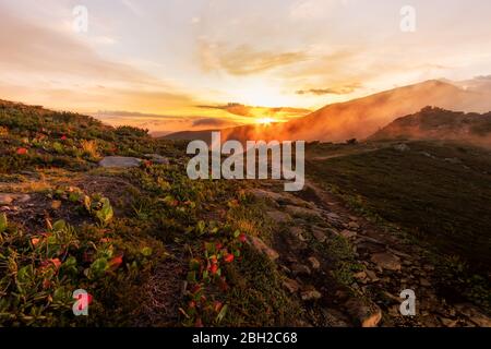 Paesaggio montano rosso-arancio alba nella nebbia e nuvole, dal sentiero alla valle. Foto Stock