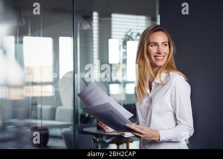 Donna d'affari sorridente che tiene i documenti in ufficio Foto Stock