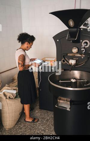 Donna che lavora in una tavoletta che utilizza la tostiera del caffè Foto Stock