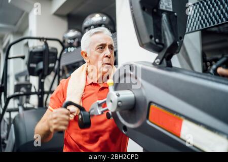 Uomo anziano che pratica alla macchina di esercitazione in palestra Foto Stock