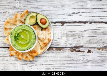 Vista dall'alto dell'avocado Hummus, fatto con ceci, avocado e tahini, con olio d'oliva. Guarnito con prezzemolo e servito con pita su un rustico Foto Stock