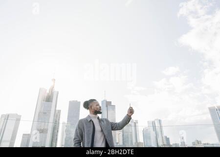 Uomo elegante sulla terrazza di osservazione che fa una foto al telefono cellulare, Francoforte, Germania Foto Stock