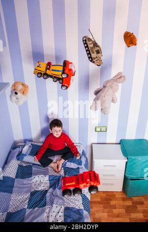 Ragazzino meditando sul suo letto con giocattoli che sorvolano la testa Foto Stock