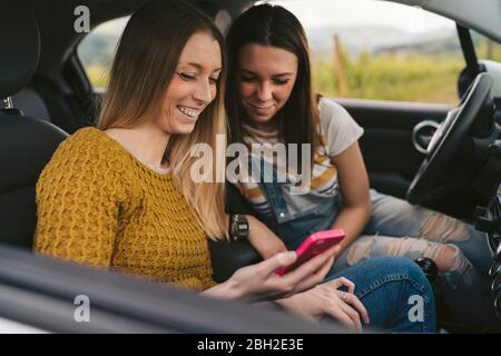 Due giovani donne felici in viaggio che condividono il telefono cellulare Foto Stock