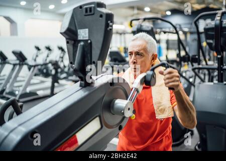 Uomo anziano che pratica alla macchina di esercitazione in palestra Foto Stock