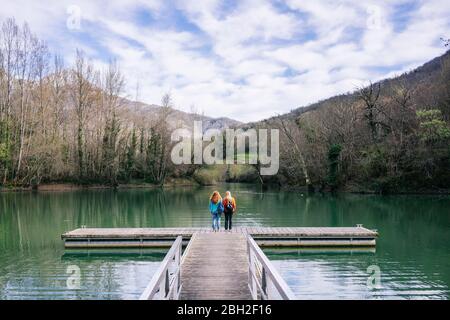 Vista posteriore di due donne con zaini in piedi sul molo, Valdemurio Reservoir, Asturias, Spagna Foto Stock