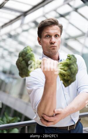 Uomo d'affari che fa l'addestramento del peso con broccoli Foto Stock