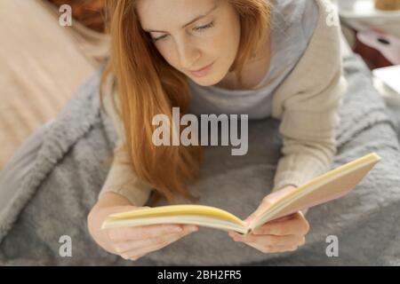 Giovane donna sdraiata su coperta di lettura notebook Foto Stock