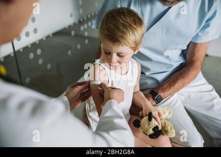 Pediatra che mette la banda-aiuto sul braccio del bambino dopo la vaccinazione Foto Stock