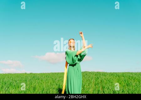 Giovane donna bendata che indossa un vestito verde in piedi in un campo Foto Stock