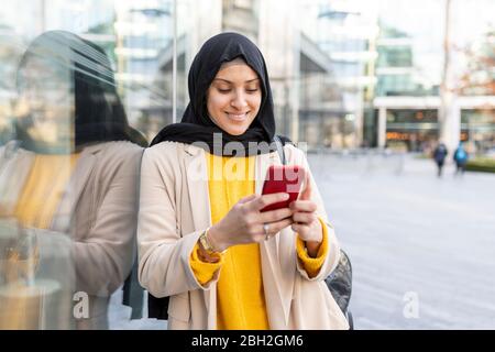 Ritratto di giovane donna sorridente che usa smartphone in città Foto Stock