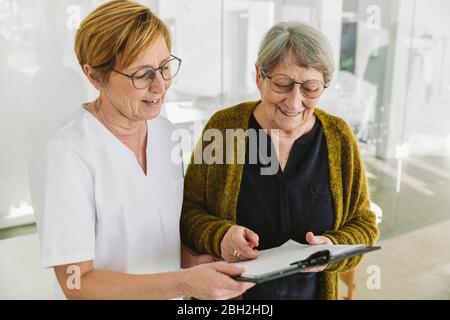 Segreteria medica per aiutare il paziente senior a compilare il documento Foto Stock