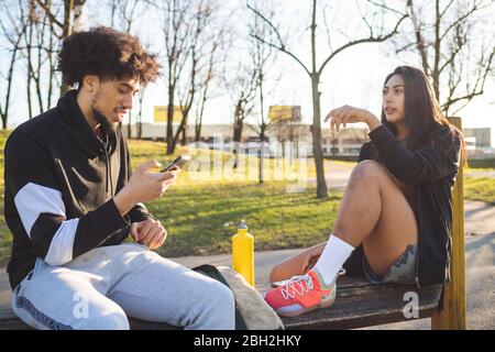 Giovane coppia sportiva che prende una pausa seduta su una panchina Foto Stock