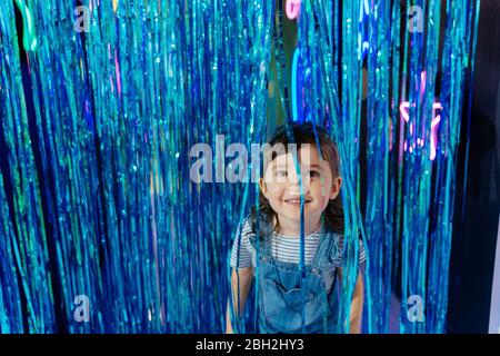 Ritratto di una bambina sorridente tra tende blu metallizzate in una sala per feste Foto Stock