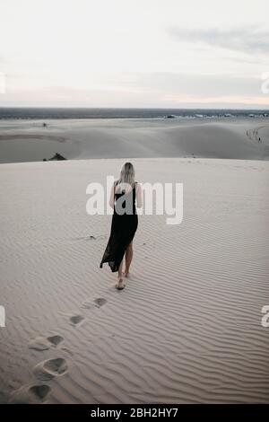 Vista posteriore di donna bionda che cammina su dune di sabbia, dune di Algodones, Brawley, USA Foto Stock