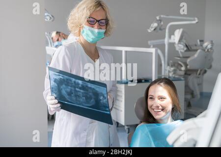 Giovane donna che ottiene il trattamento dentale in clinica, medico che spiega la radiografia Foto Stock