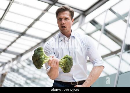 Uomo d'affari che fa l'addestramento del peso con broccoli Foto Stock