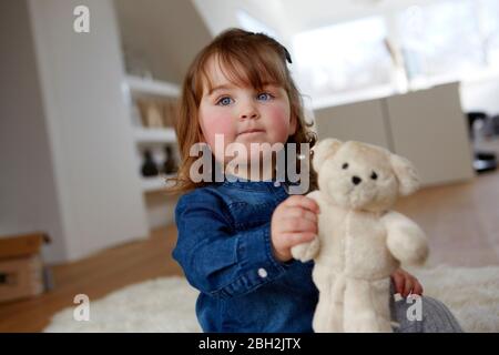 Ritratto di bambina con orsacchiotto seduto sul pavimento a casa Foto Stock