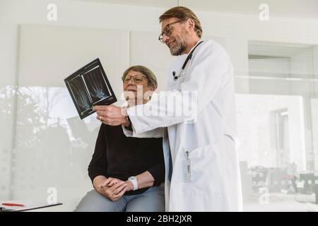 Medico che discute l'immagine radiografica della mano rotta con il paziente anziano Foto Stock