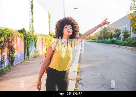 Giovane donna con afro hairdo hitchtrekking in città Foto Stock