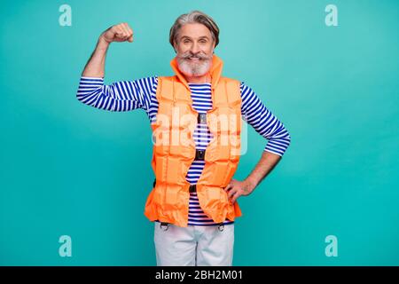 Foto di attraente uomo anziano mostra big bicips braccio forte marinaio bagnino mare oceano viaggio indossare a righe marinaio camicia pantaloncini arancione giubbotto sicuro Foto Stock