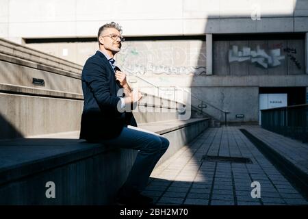 Uomo d'affari dai capelli grigi seduto sulle scale all'aperto Foto Stock
