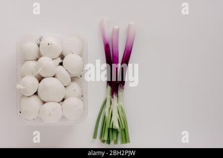 Funghi freschi anfroni bianchi in plastica e cipolle verdi scalogni o scalogno su fondo bianco. Foto Stock