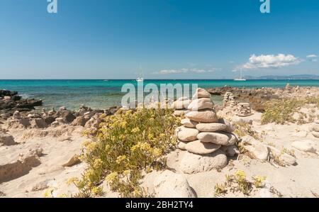 Vista panoramica su una spiaggia di sabbia e roccia. Sullo sfondo il mare mediterraneo con barche a vela ormeggiate nella tranquilla baia di Formentera, Baleari Foto Stock